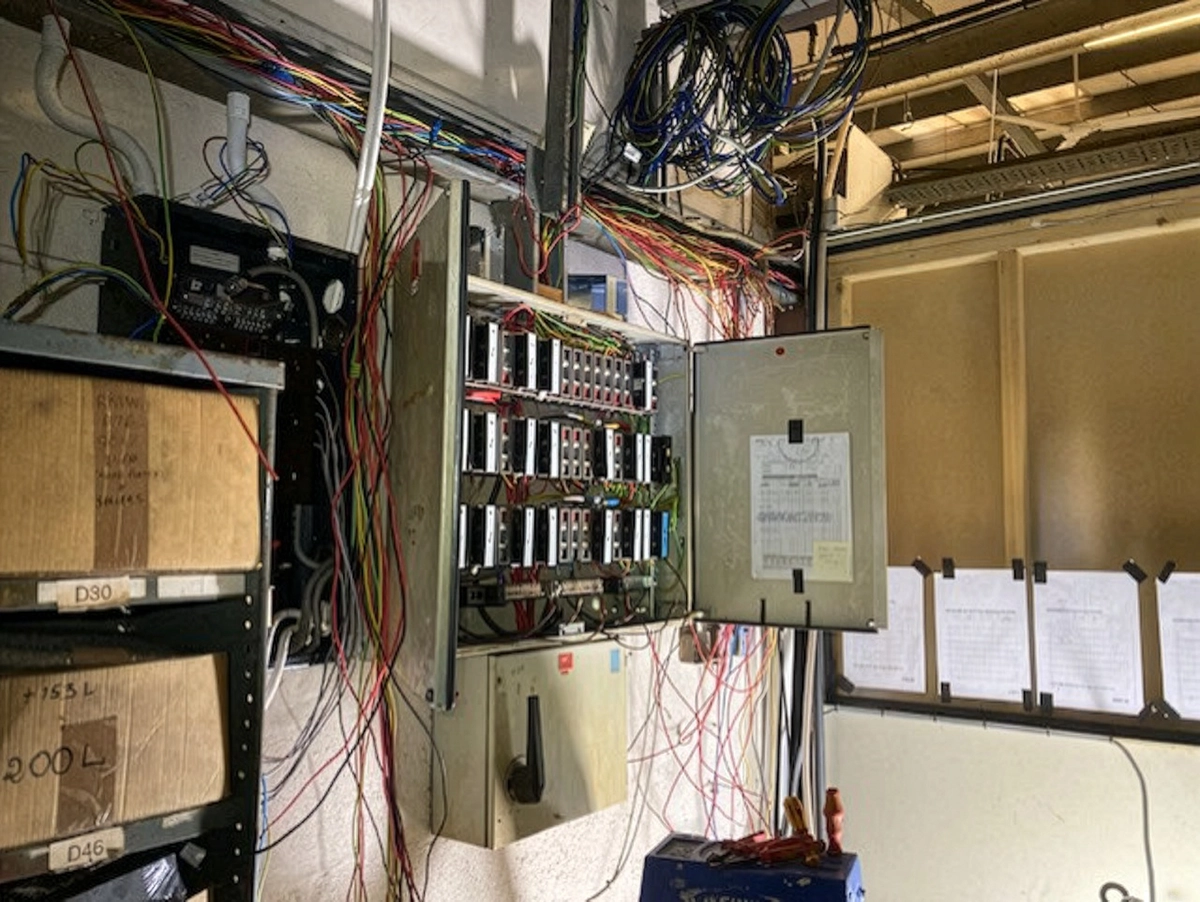 Open industrial electrical box with many tangled coloured wires hanging out.